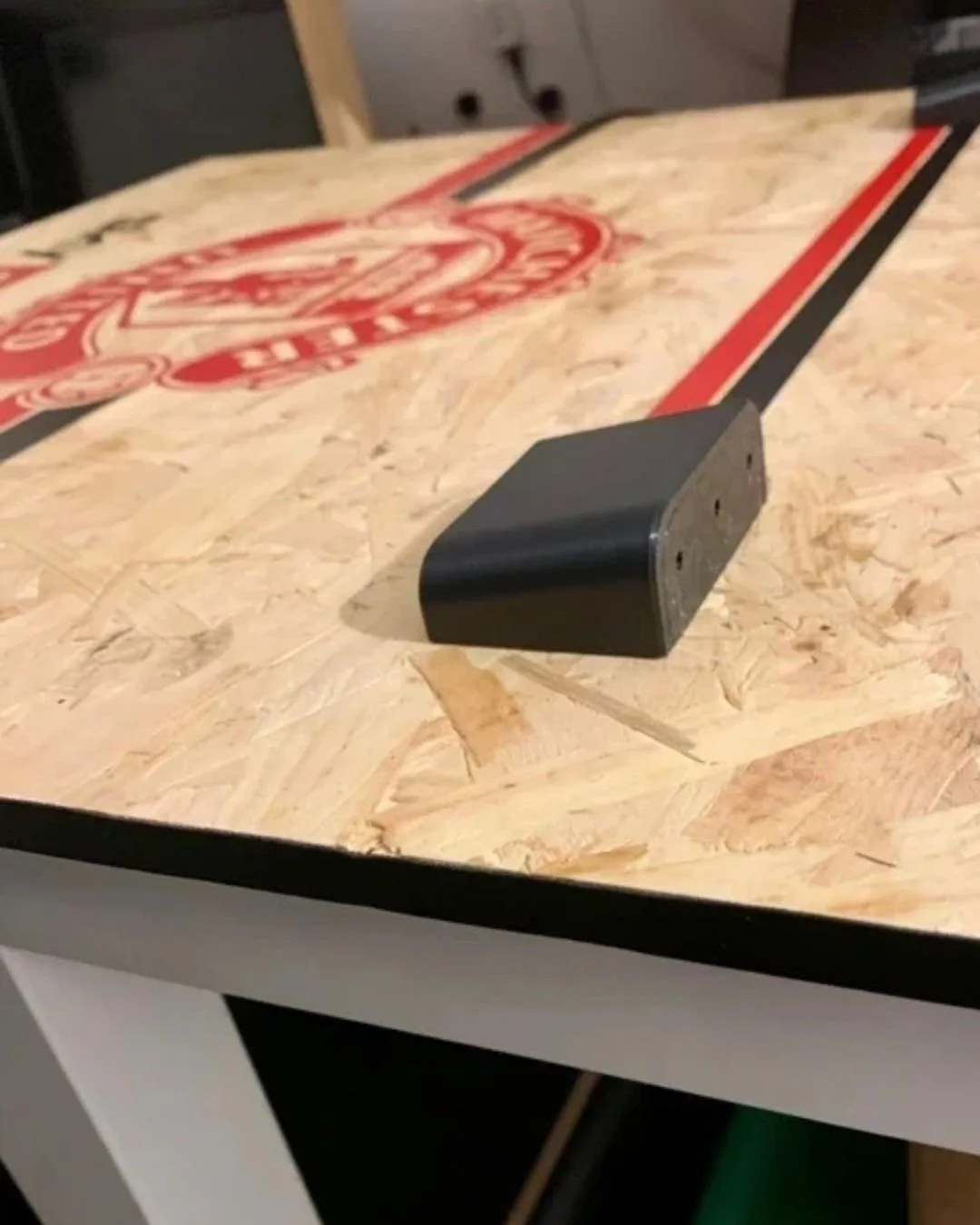 Close-up of a hockey puck resting on a wooden table with sports team logo and red and black lines.