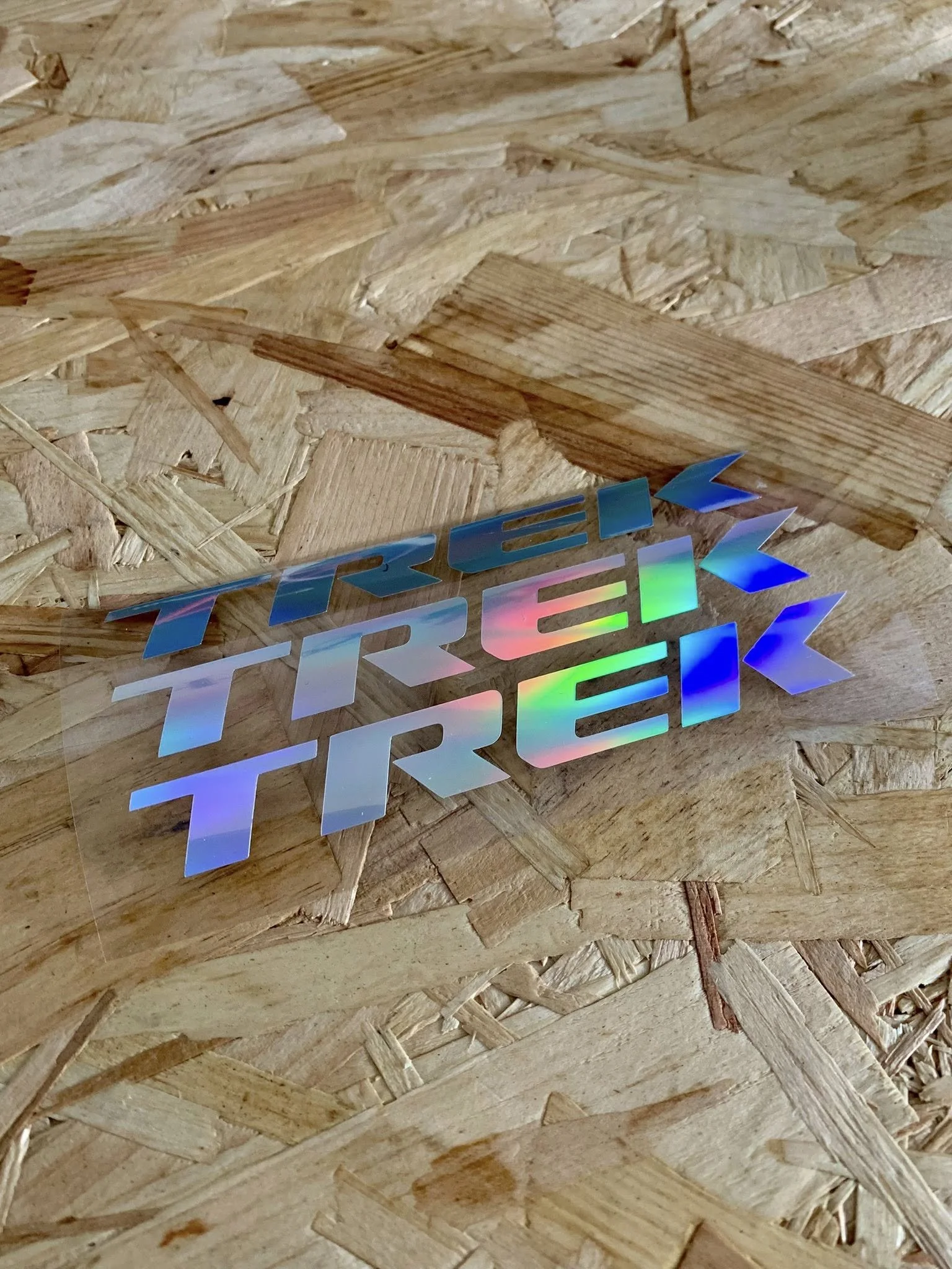 Close-up of a holographic sticker on a wooden surface, with colorful, reflective text that is partially visible.