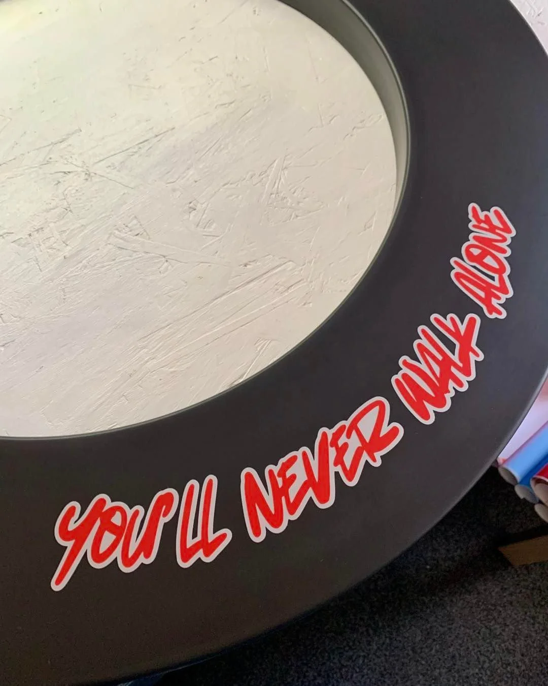 Close-up of a circular mirror with a message on the rim that reads, 'You'll never look alone' in red and white text.