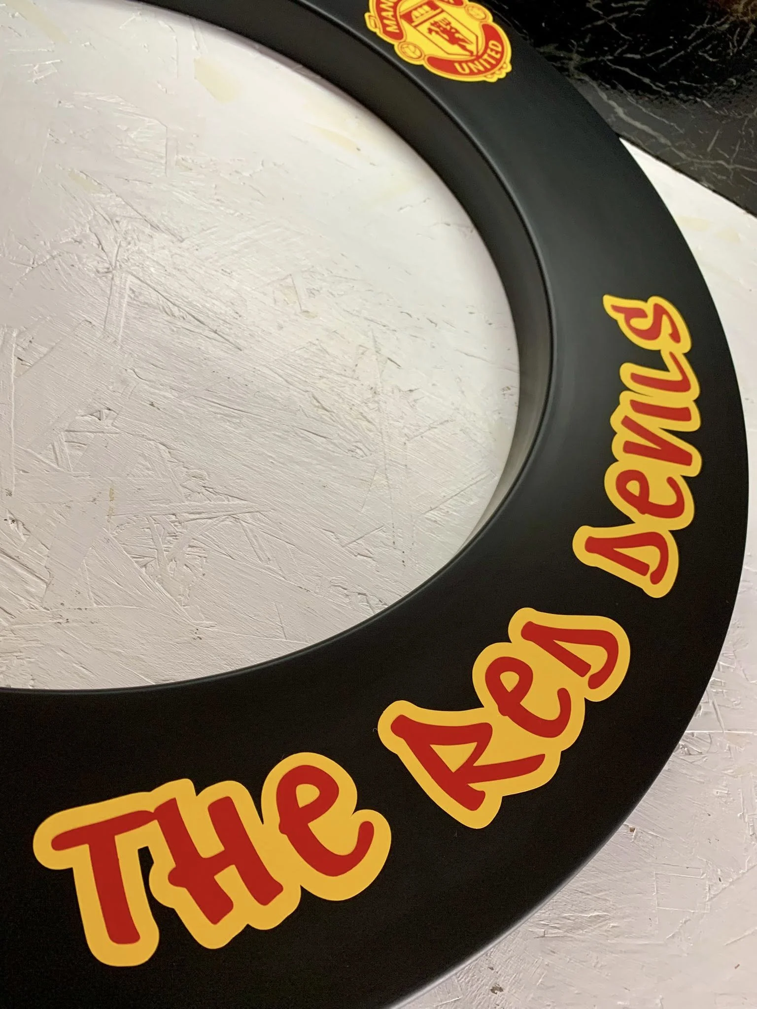 Close-up of a circular sign with a red and yellow logo of Manchester United and partially visible text on a black background.