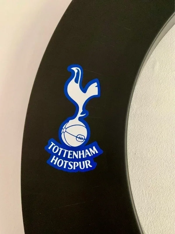 Close-up of a black curved surface with a Tottenham Hotspur football club logo, featuring a cockerel standing on a football, and the club's name in blue and white.