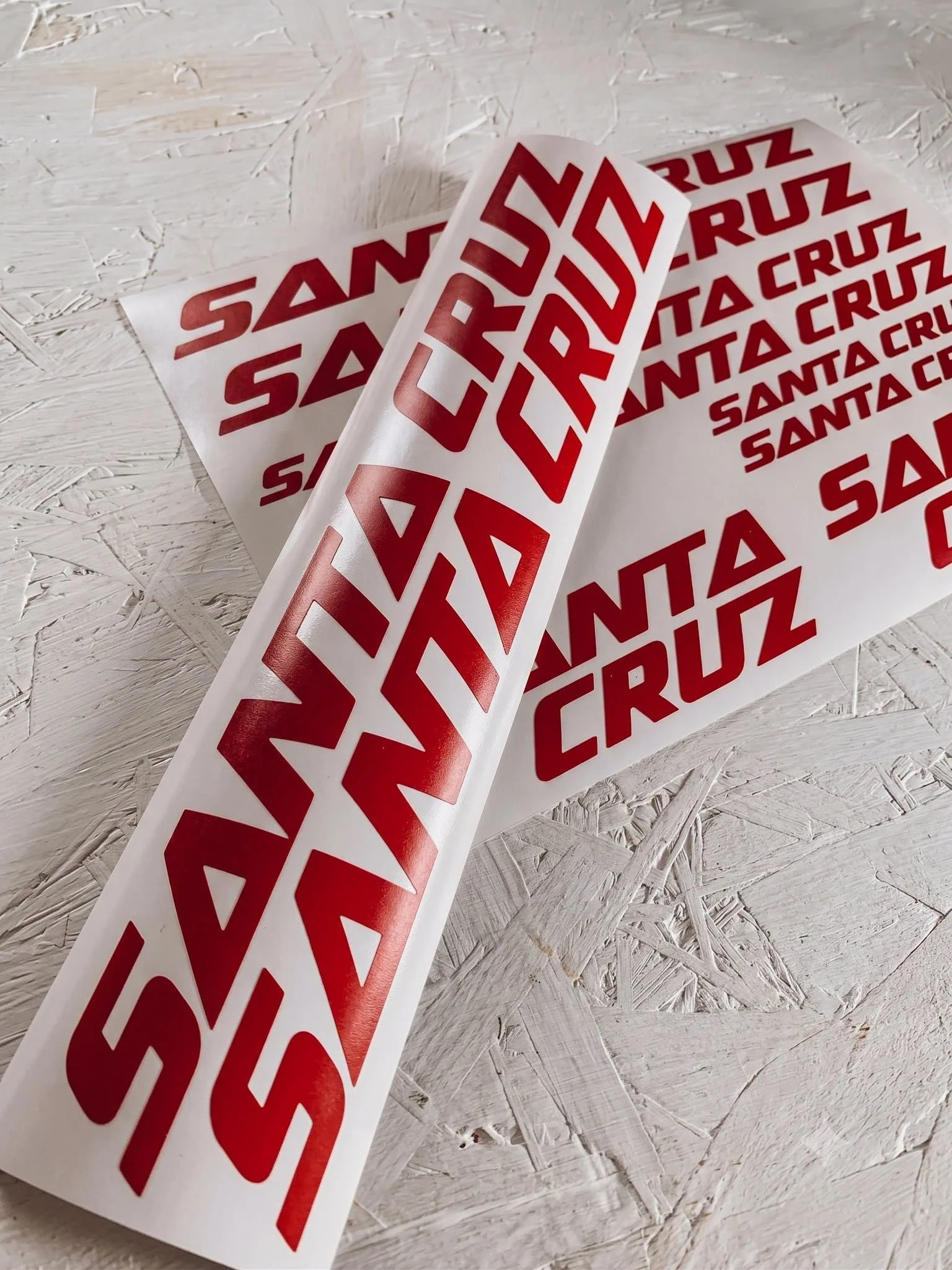 Three sheets of red and white stickers with the text 'SANTA CRUZ' on a textured white surface.
