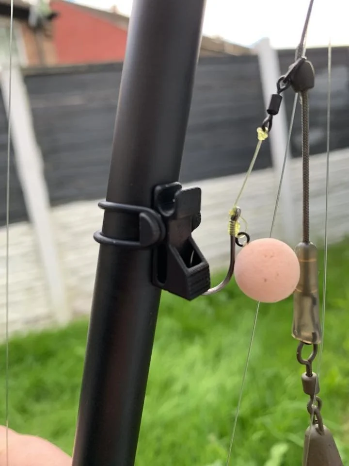 Close-up of fishing rod with lure, float, and line in a backyard with grass and a wooden fence in the background.