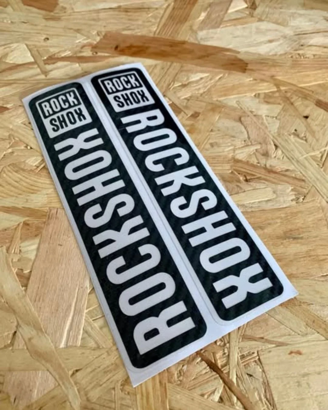 Two identical Rock Shox stickers on a wooden surface.