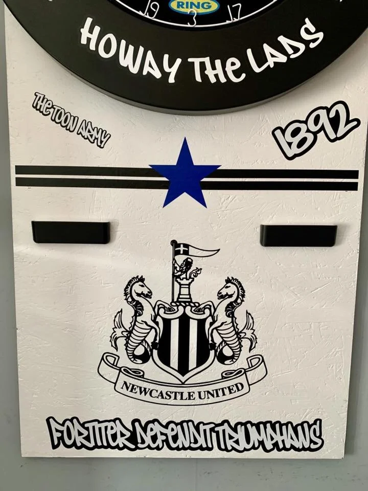 A wall calendar with a Newcastle United football club crest and various texts, including 'HOWAY THE LADS,' '1892,' and 'FOURTEEN POINTS TERMINOLOGY.' The calendar features black and white colors with some text in different fonts, and a blue star is l