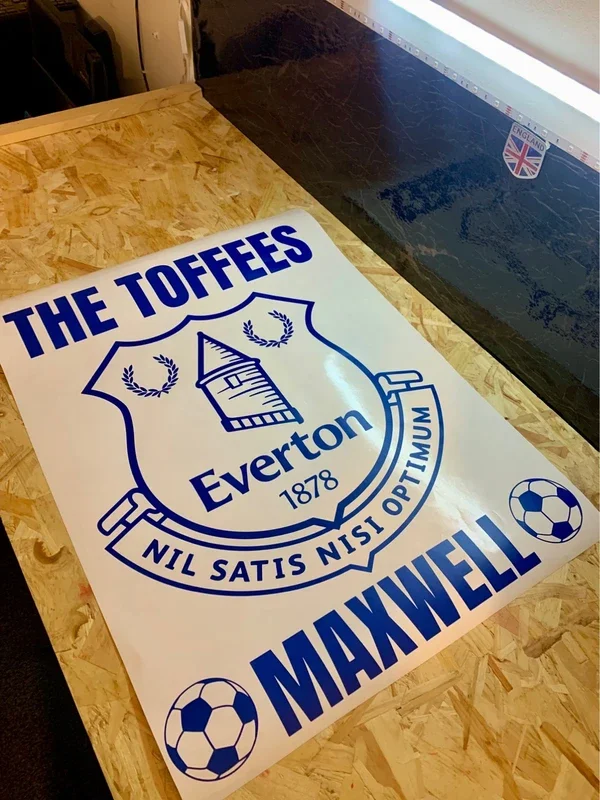 A white poster with blue text and graphics of a crest, two soccer balls, and the words "The Toffees," "Everton 1878," "Nil Satis Nisi Optimum" along with the name "Maxwell."