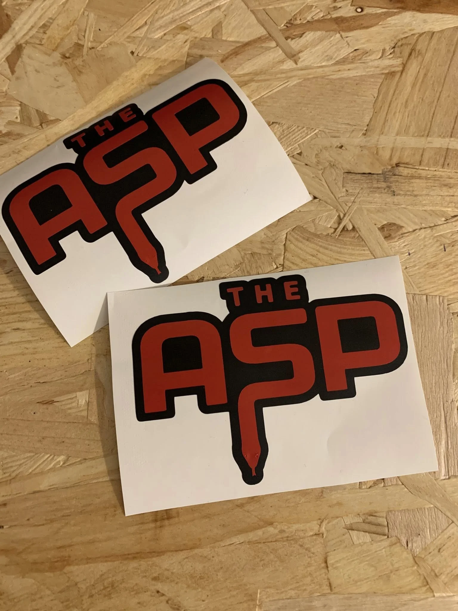 Two stickers on a wooden surface with the text 'THE 52 P' in bold, red and black font.