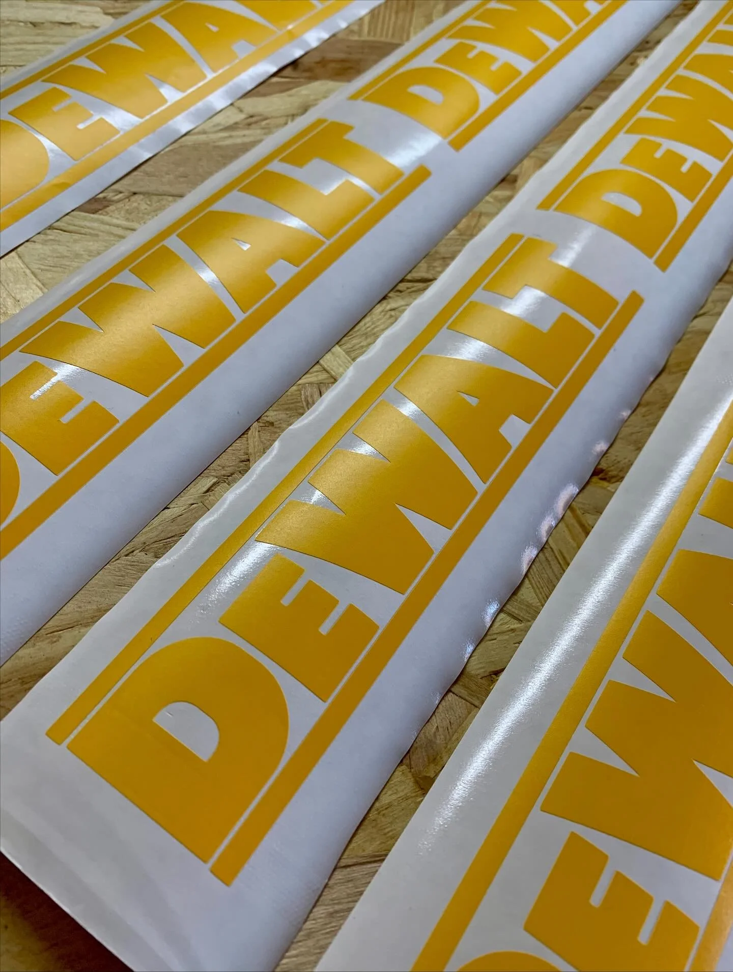 Close-up of large yellow and white decals with the text 'DEALER' printed on them, laid out on a wooden surface.