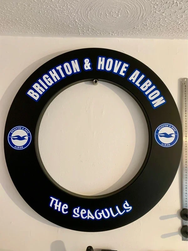 A large round black wreath with blue text and logos for Brighton & Hove Albion football team, featuring the team name and a seagull mascot, hanging on a white wall.
