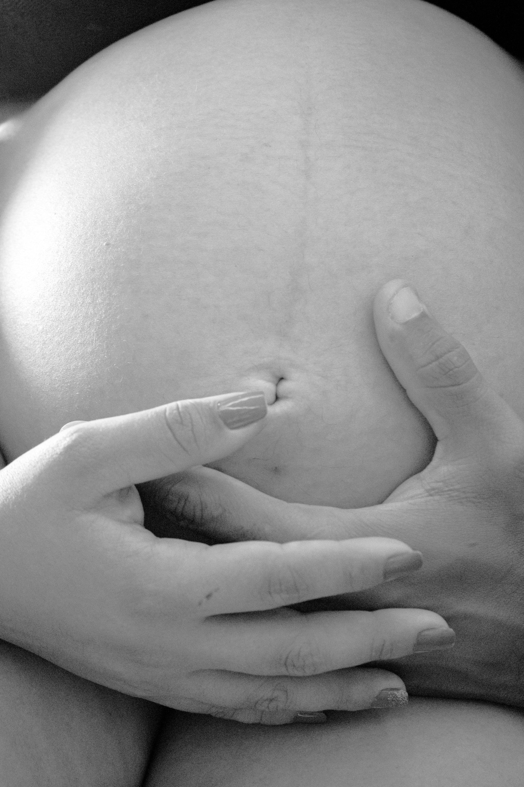 Close-up black and white photo of a person’s hand touching their belly, with the thumb and fingers gently resting on the skin.