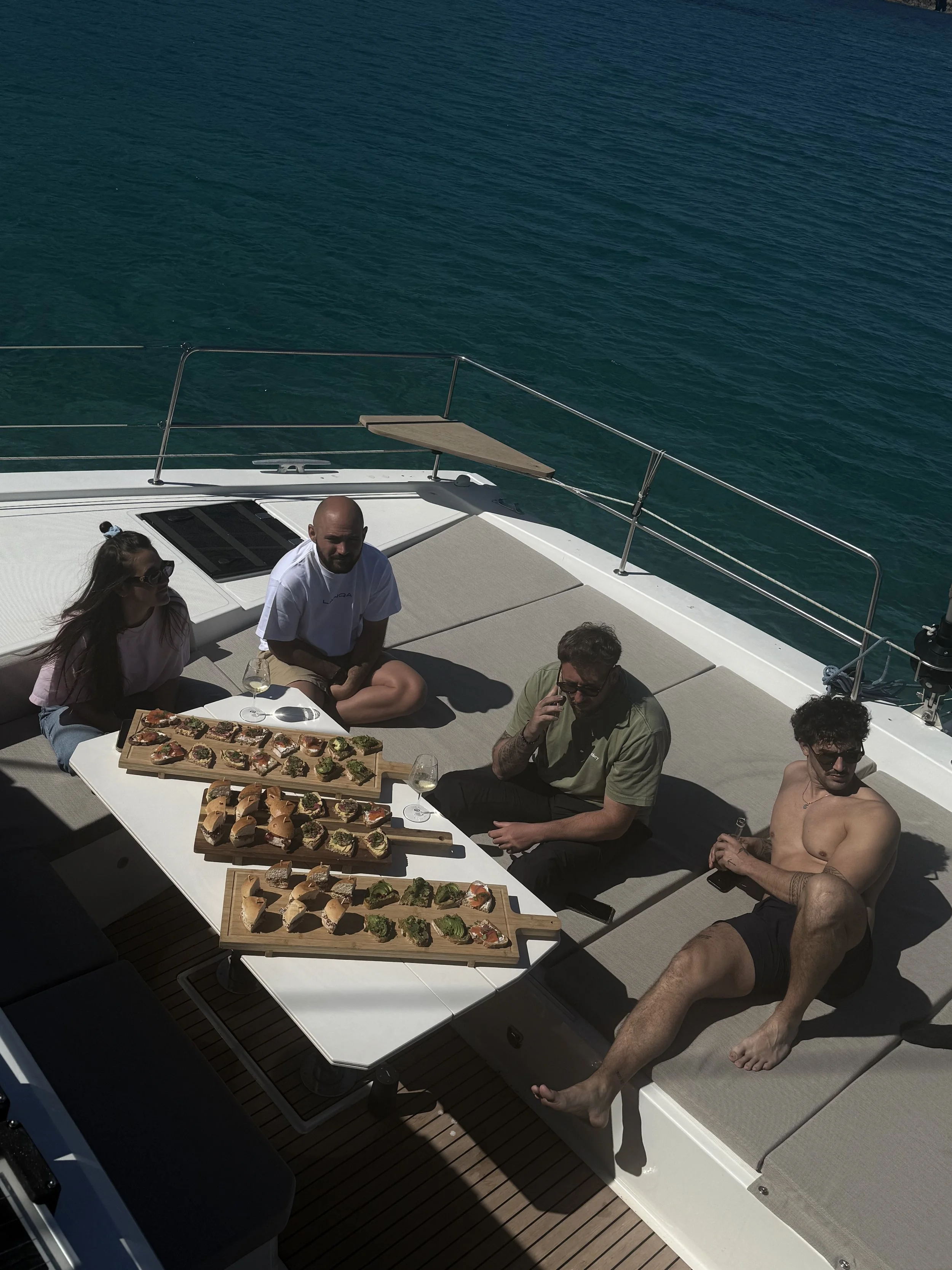Groupe de quatre personnes assises sur  catamaran Bali 4.6 avec un plateau de nourriture et de boissons, en mer lors d'une journée ensoleillée.