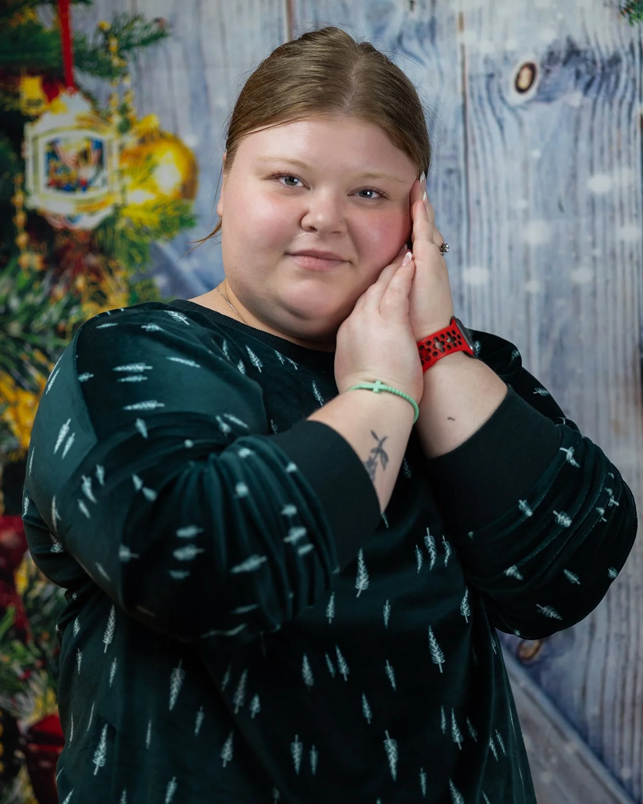 A woman with her hands gently pressed against her right cheek, wearing a black shirt with white patterns, a red watch, and a green bracelet.