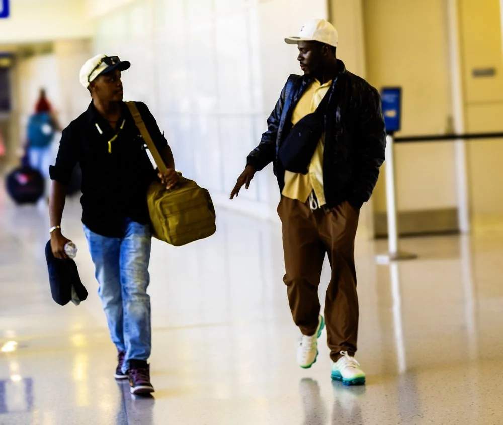 Two men walking in an airport terminal carrying bags and wearing hats.