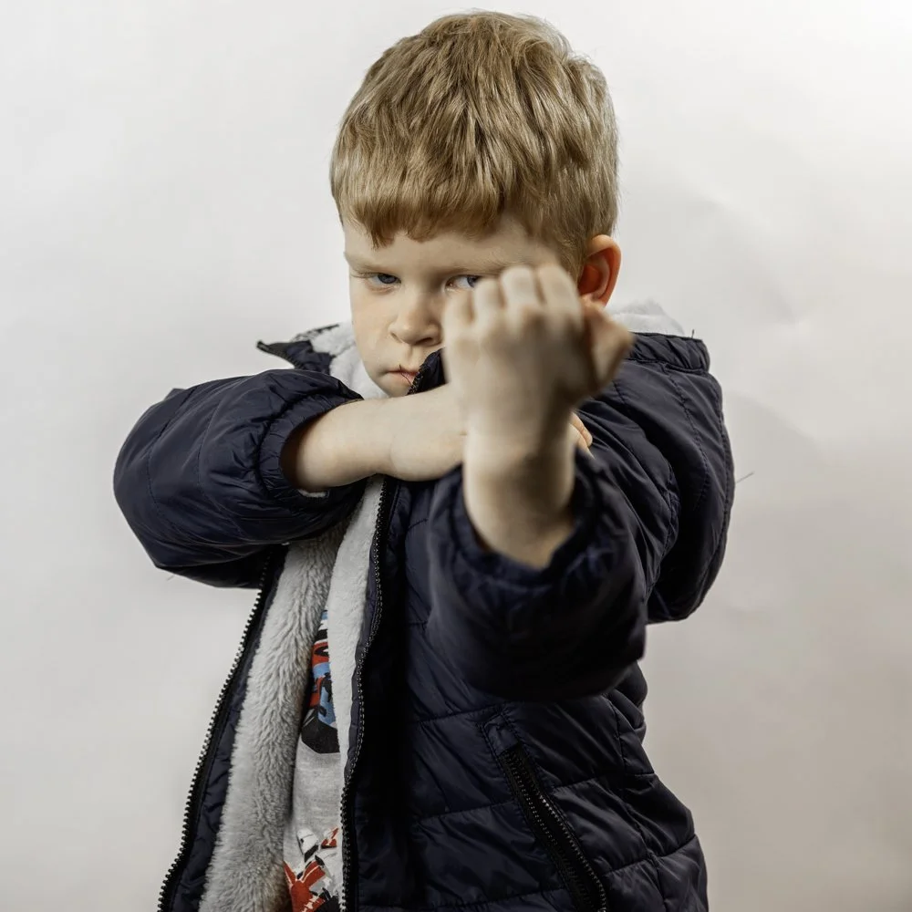 A young boy with red hair in a fighting stance, wearing a black jacket, against a plain white background.