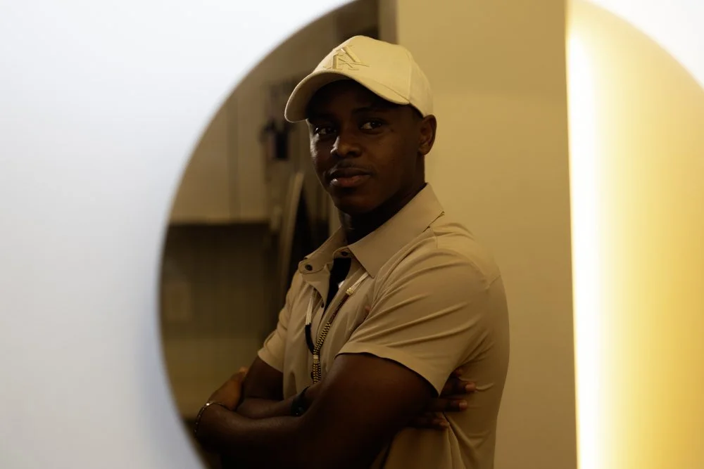 A man in a beige uniform and cap, standing with arms crossed, seen through a circular opening in the foreground.