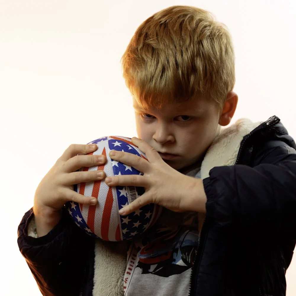 A young boy with red hair holding a basketball decorated with the American flag.