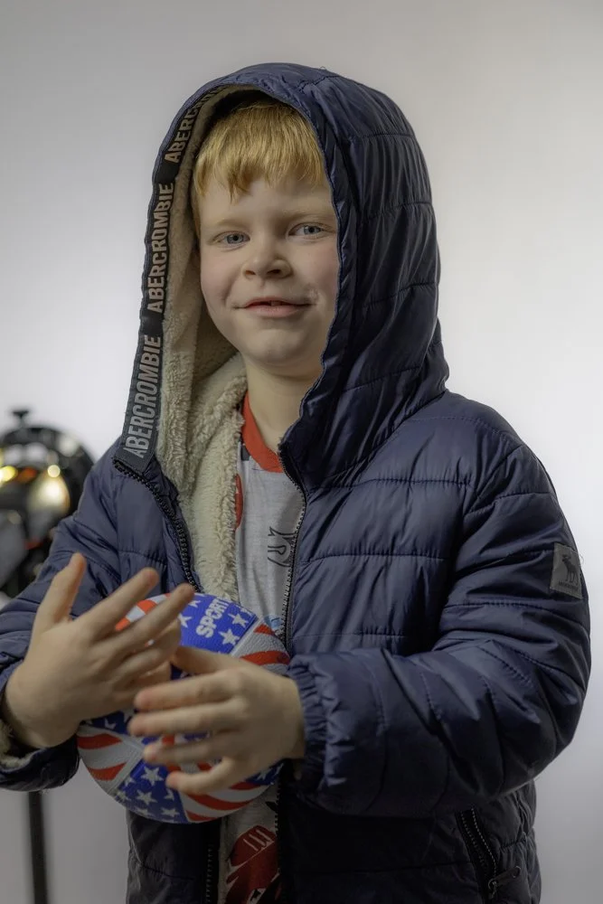 A young boy with red hair wearing a navy blue puffy jacket holding a decorated football.