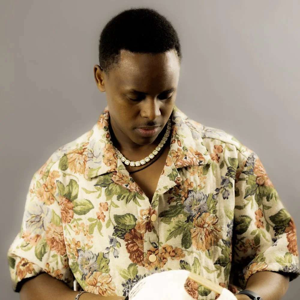 A woman with short hair wearing a floral shirt and pearl necklace looking down.