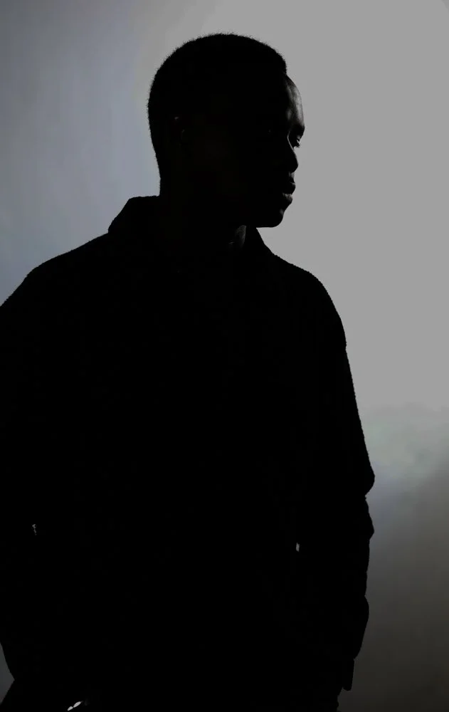 Silhouette of a young man with short hair, wearing a hoodie, standing against a light background.
