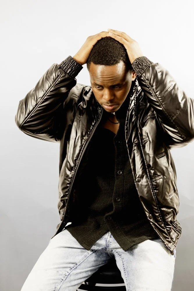 Man in a shiny black jacket holding his head with both hands, looking down thoughtfully