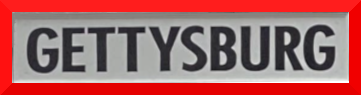 Close-up of a sign reading 'GETTYSBURG' in bold black letters on a gray background with a red border.