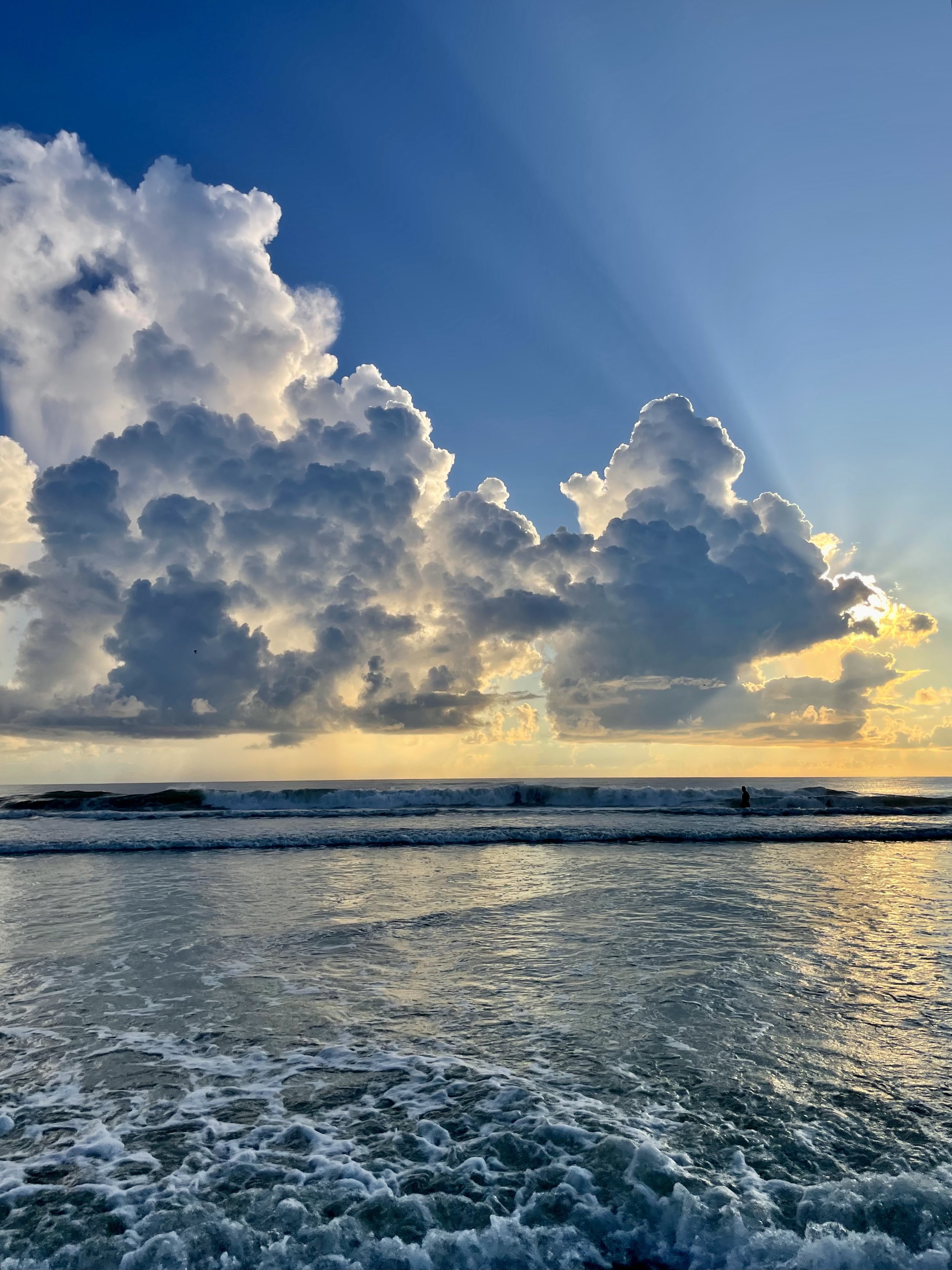 Sunrise over the ocean with large clouds and a swimmer in the water.