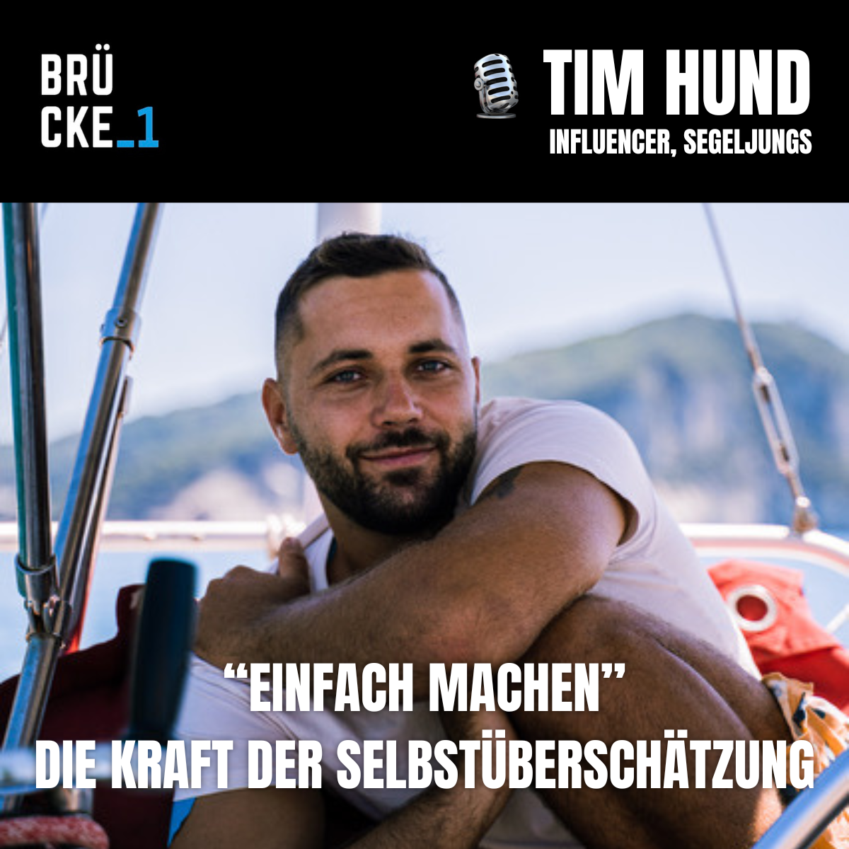 Ein Mann sitzt auf einem Segelboot mit Blick auf das Meer und Berge im Hintergrund, lächelnd in die Kamera.