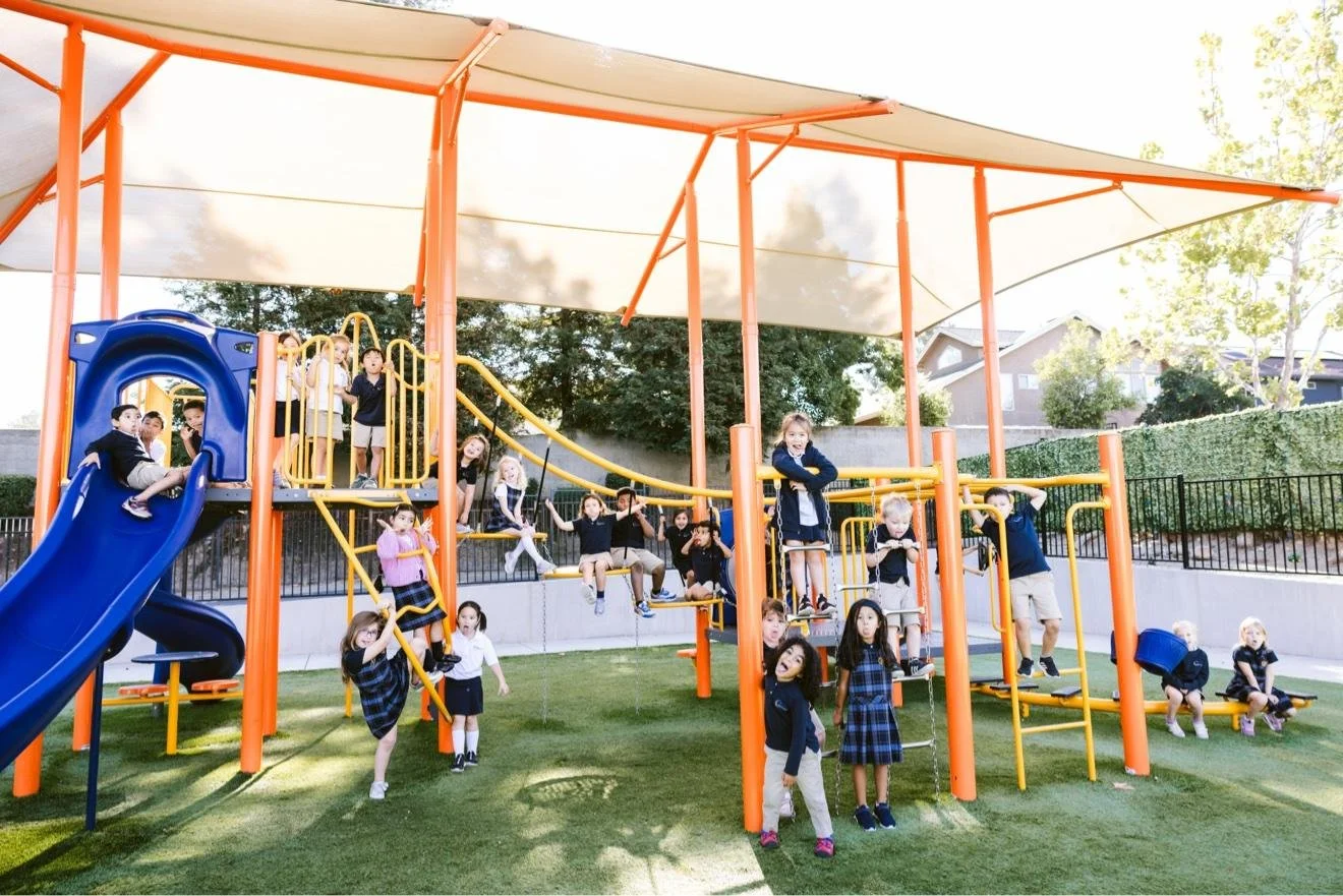 Students playing on a shaded playground with a slide