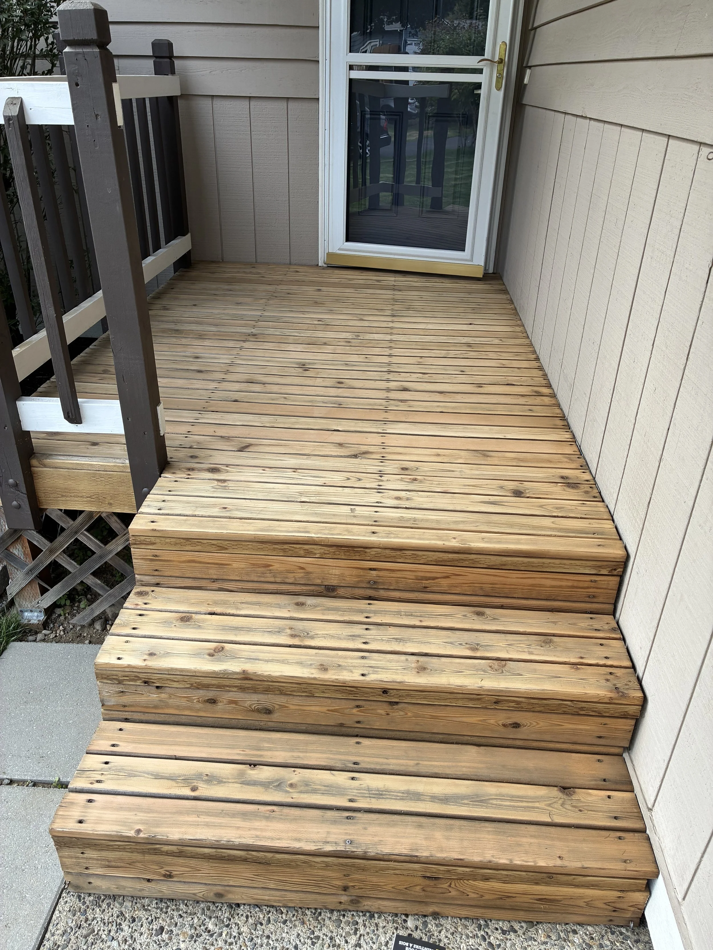 Wooden steps leading up to a screened door on a porch with beige siding.