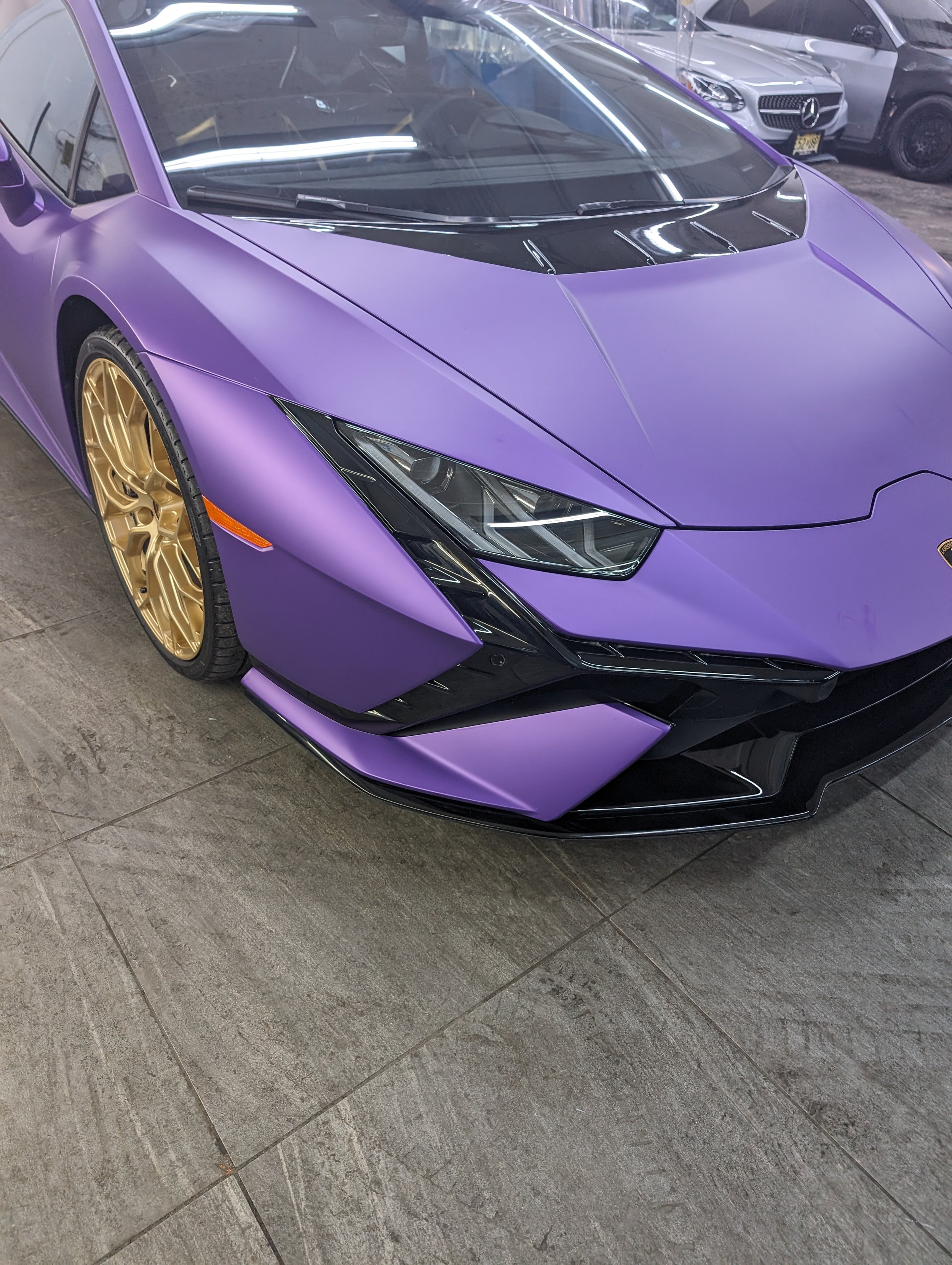 Purple sports car with gold wheels and sleek design, parked indoors.