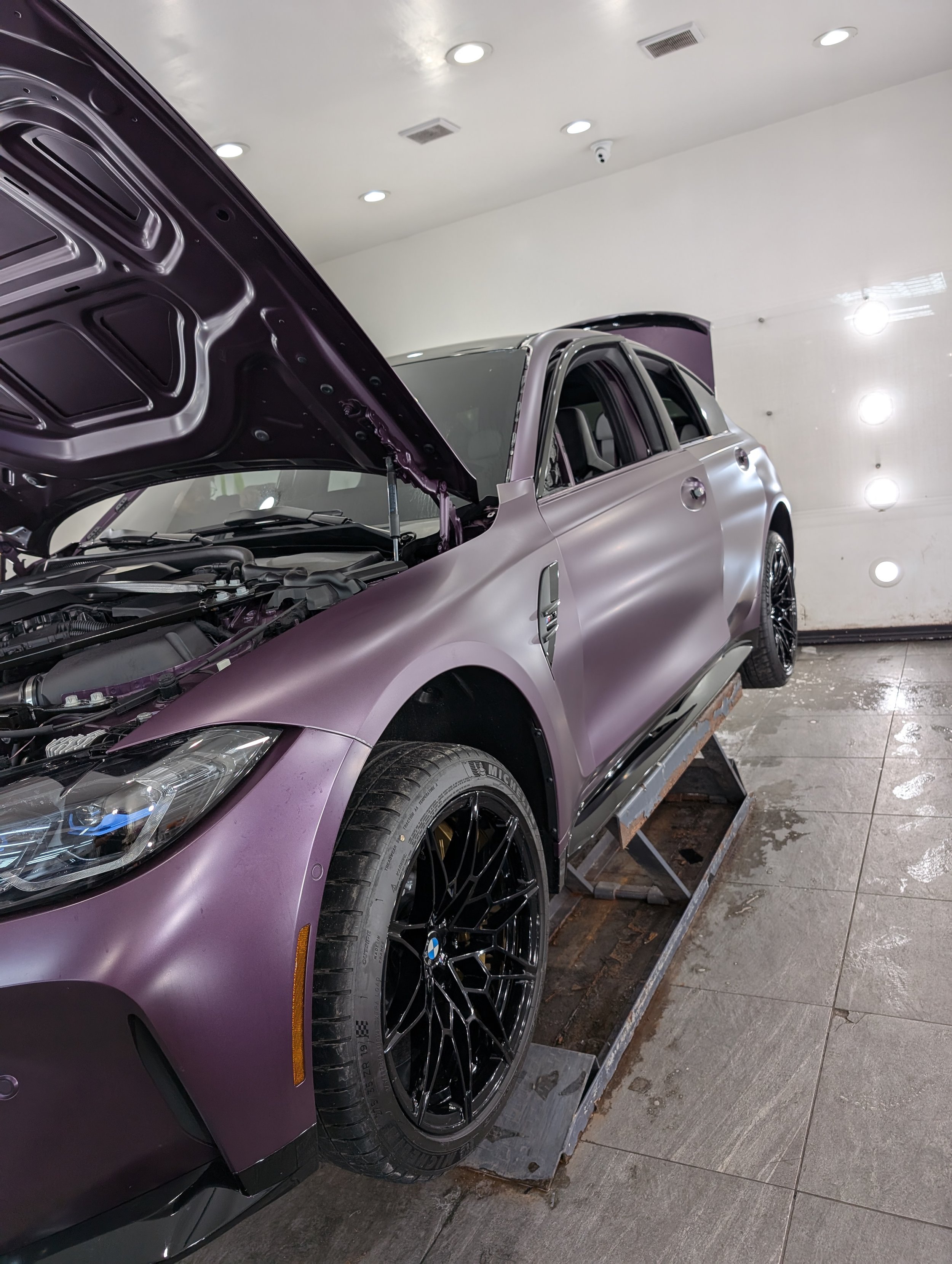 Purple BMW SUV on a car lift with open hood and doors in a garage.