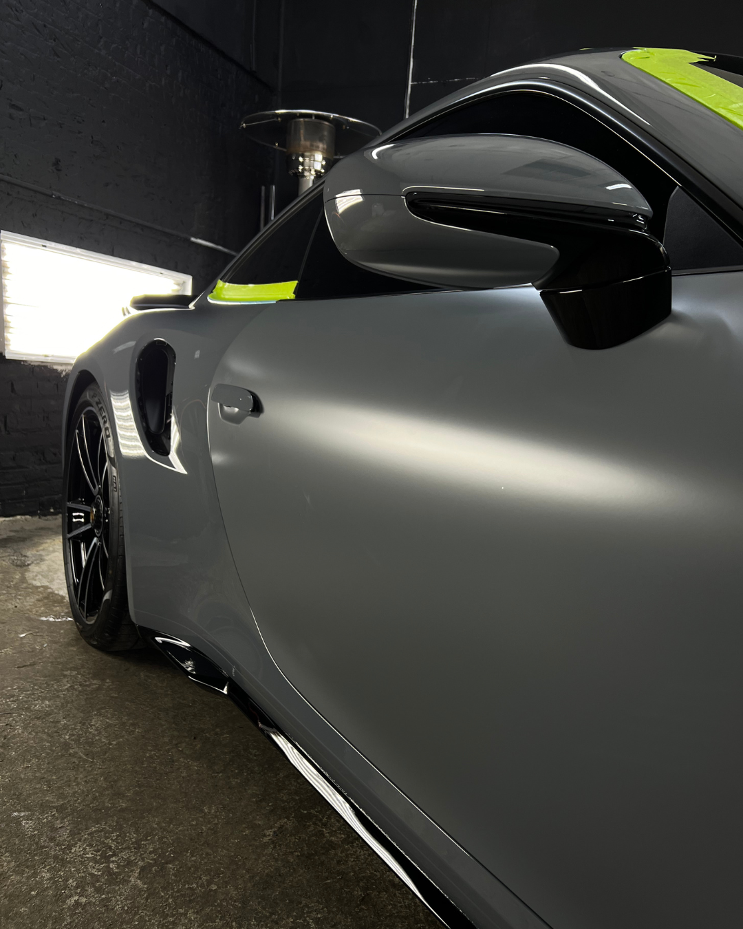 Close-up of a sleek gray sports car with a side mirror and wheel, set indoors.