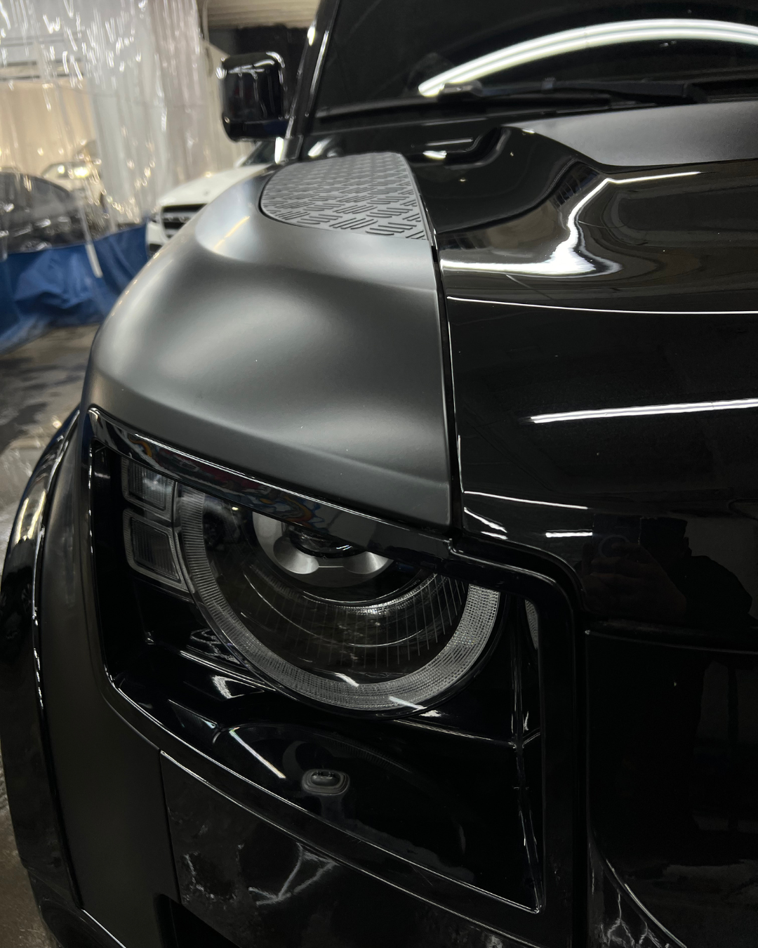 Close-up of a black car's front headlight and hood in a garage setting.