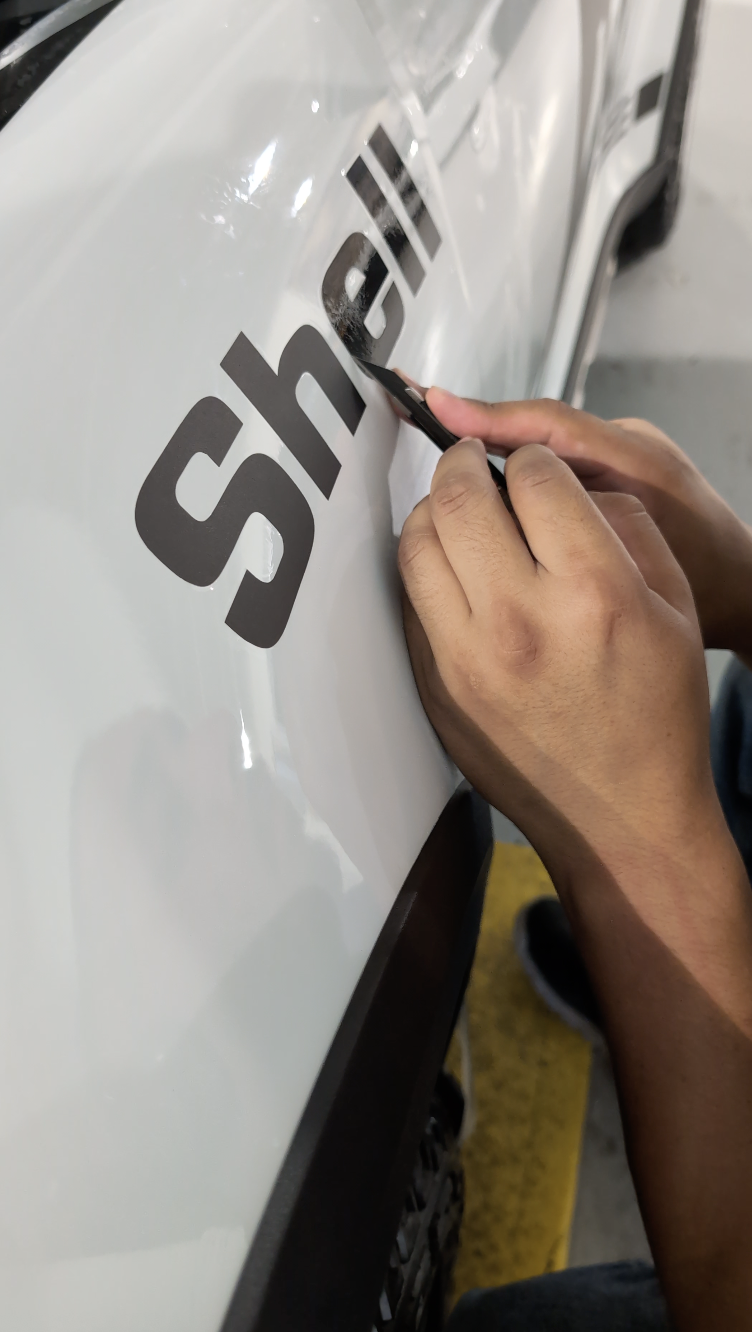 Person peeling decal off white surface with a tool