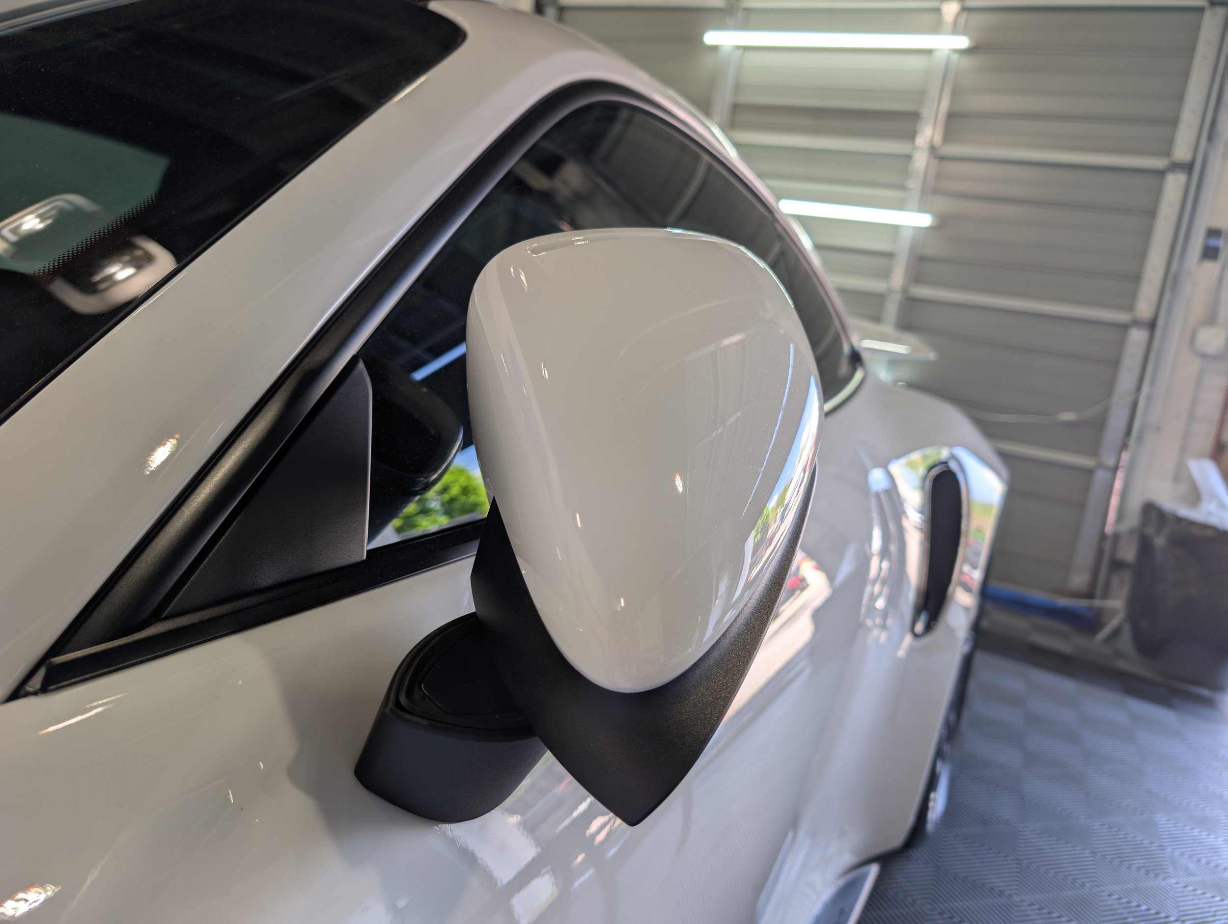 Side view of white car's rearview mirror in a garage.