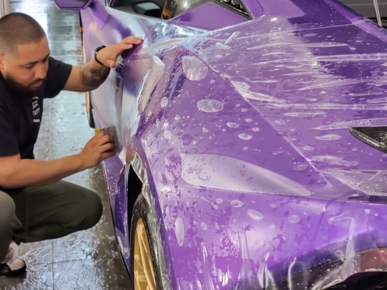 Man applying protective film to a purple sports car