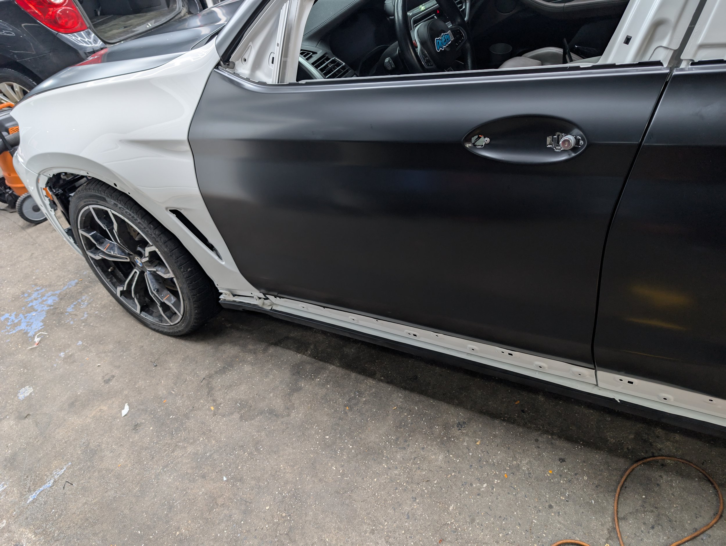 A vehicle undergoing repair with parts disassembled, showing a partially attached door and exposed interior.