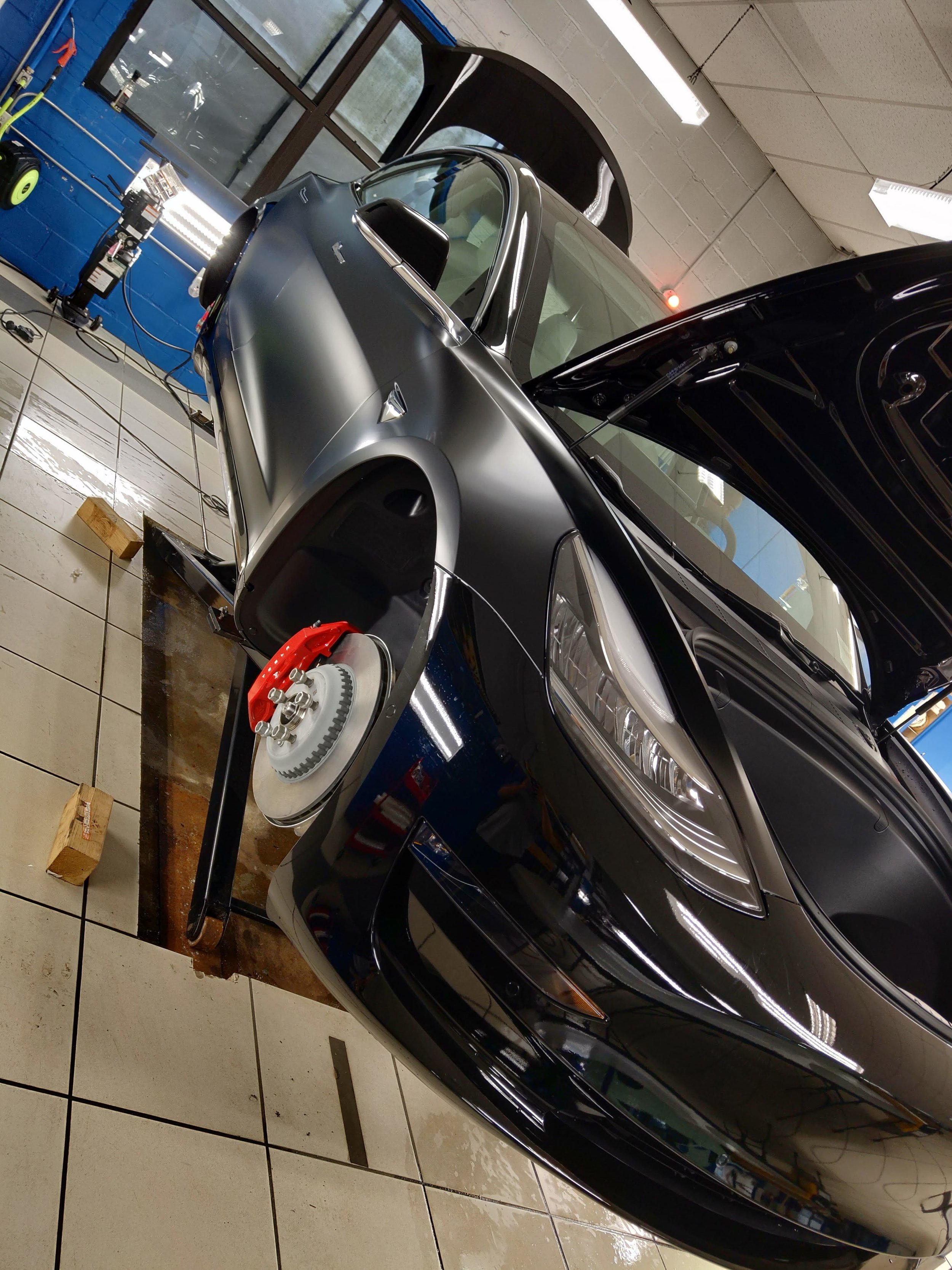 A black car lifted in a garage with its front wheel removed and hood open.