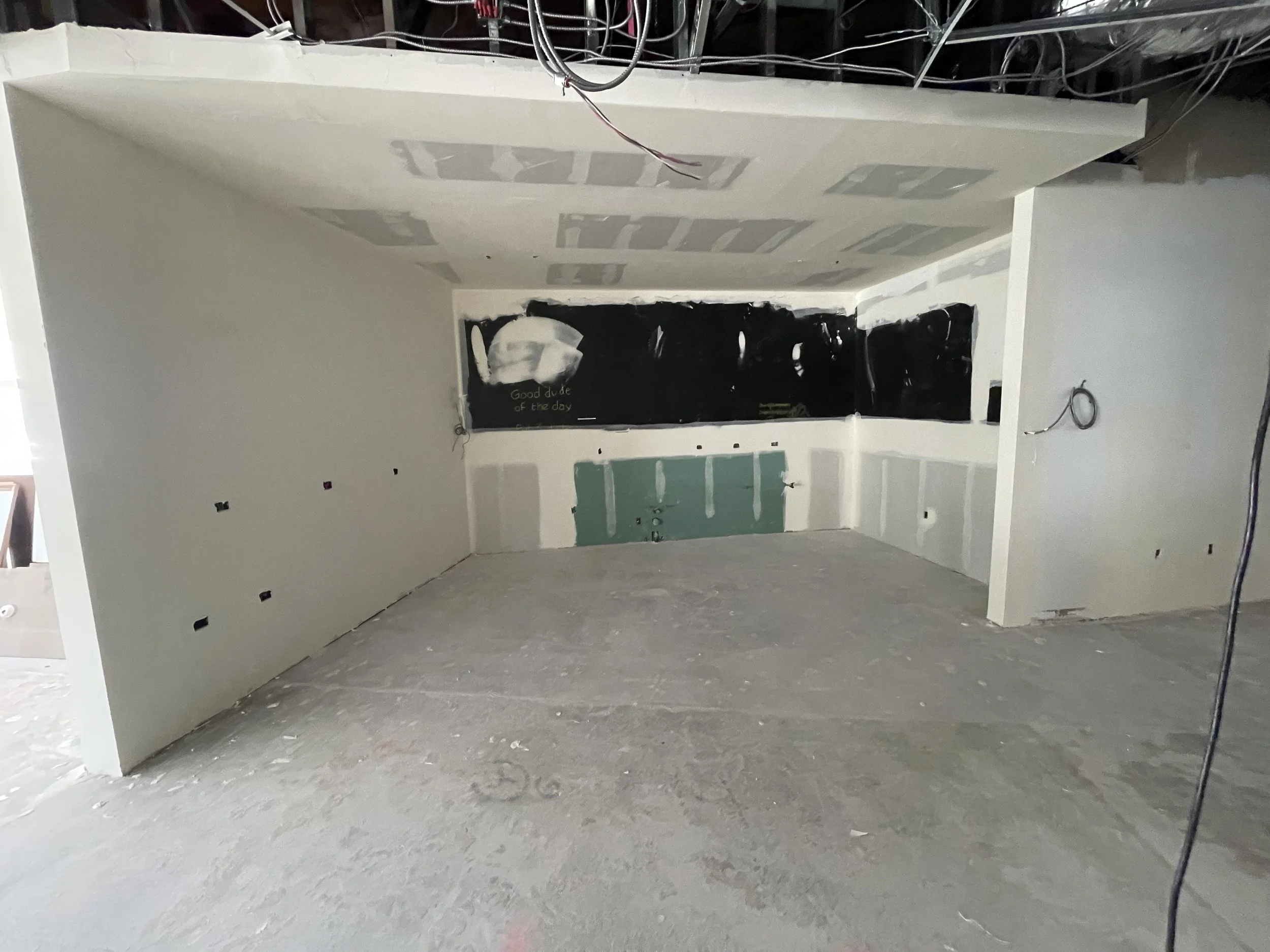 Interior of a room under construction with unfinished drywall, visible electrical wiring, and a black chalkboard wall with some writing and drawings.