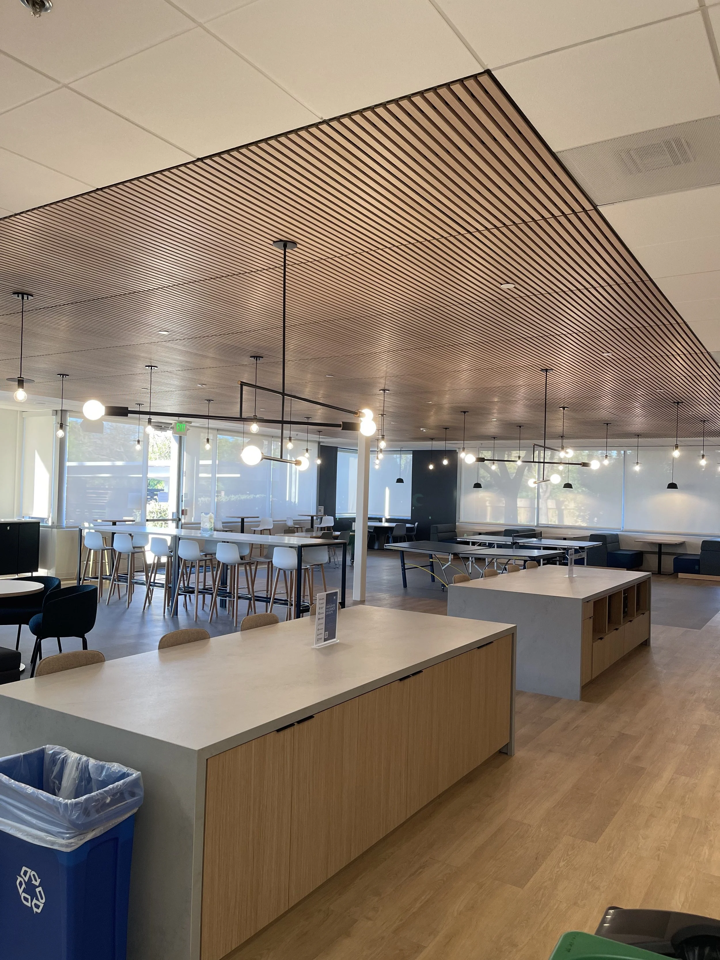 Interior of a modern cafe or lounge with tables, chairs, large windows, and hanging lights.