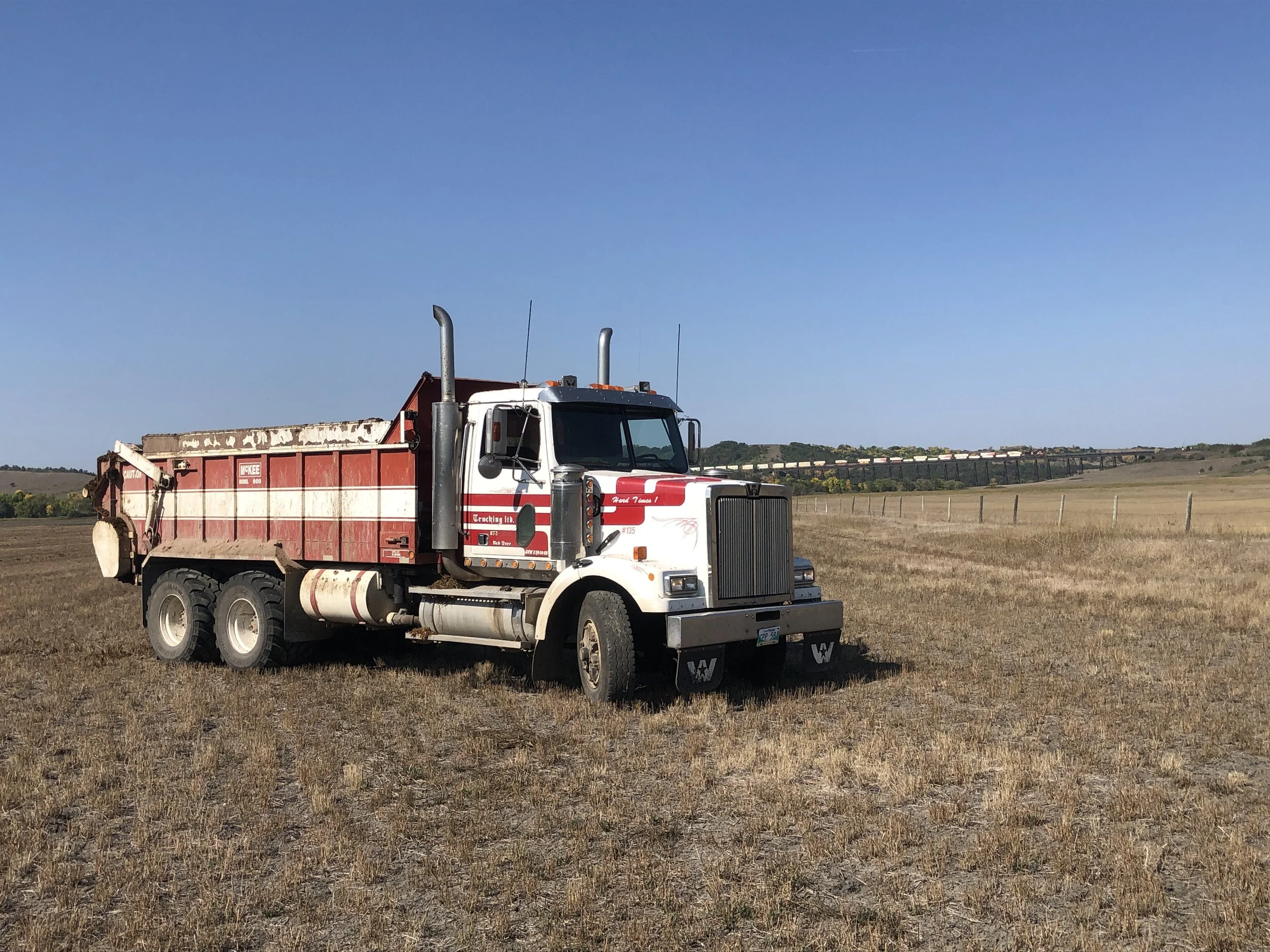 A red and white dump truck parked in an open field under a clear blue sky.