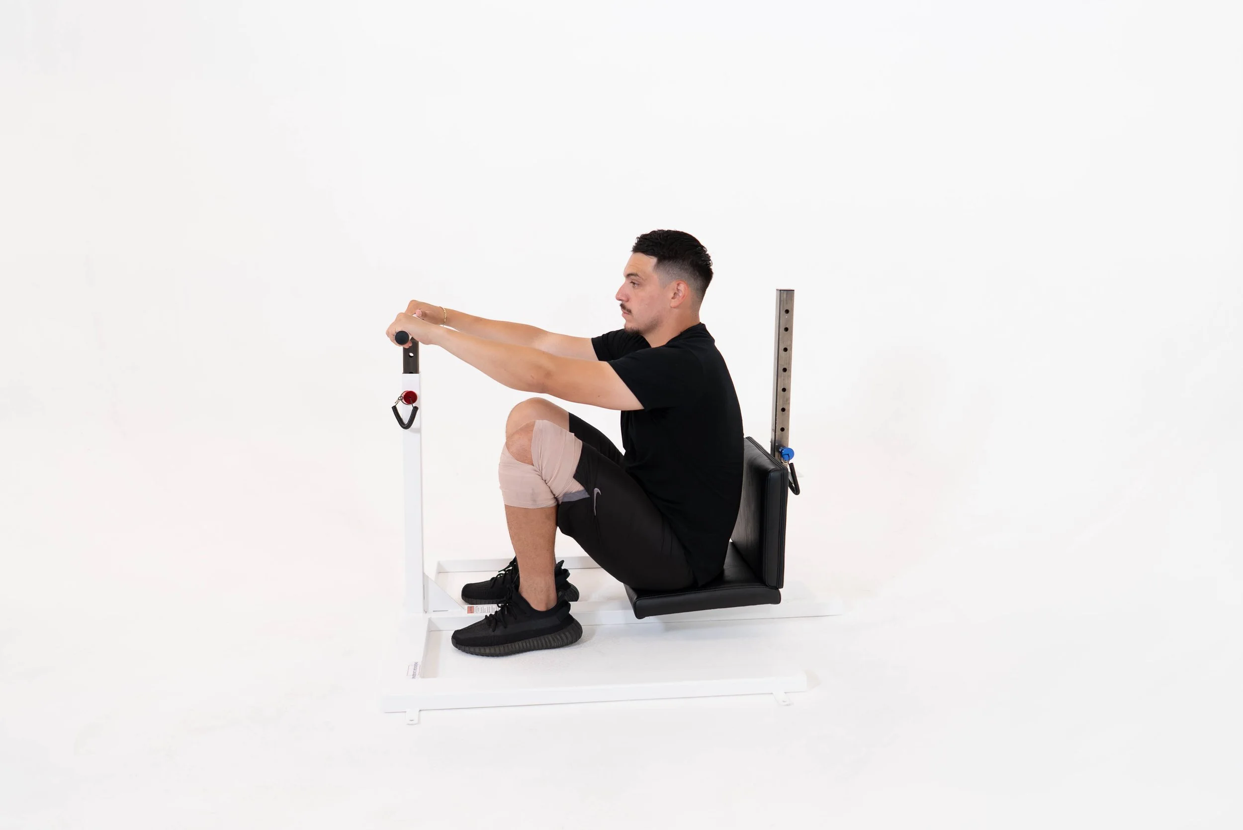 A man exercising on a specialized seated stretching machine in a white studio.