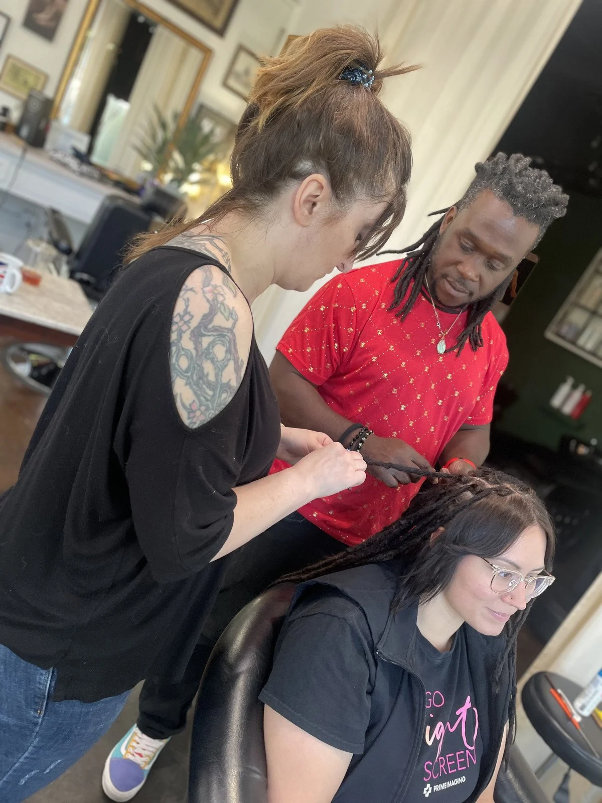 A bright modern studio space with large windows, white desk, black swivel chairs, and various office supplies on the desk.