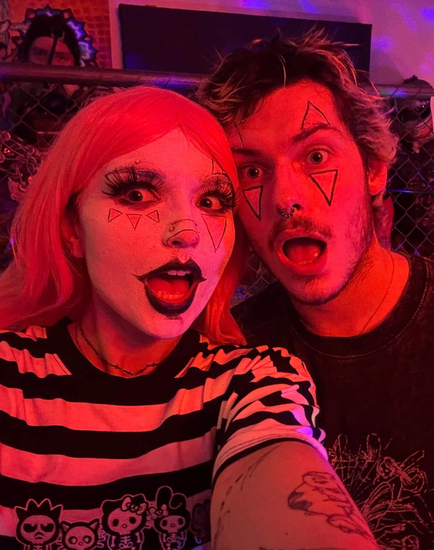 People taking a selfie with face paint and makeup, illuminated by red and purple lighting.