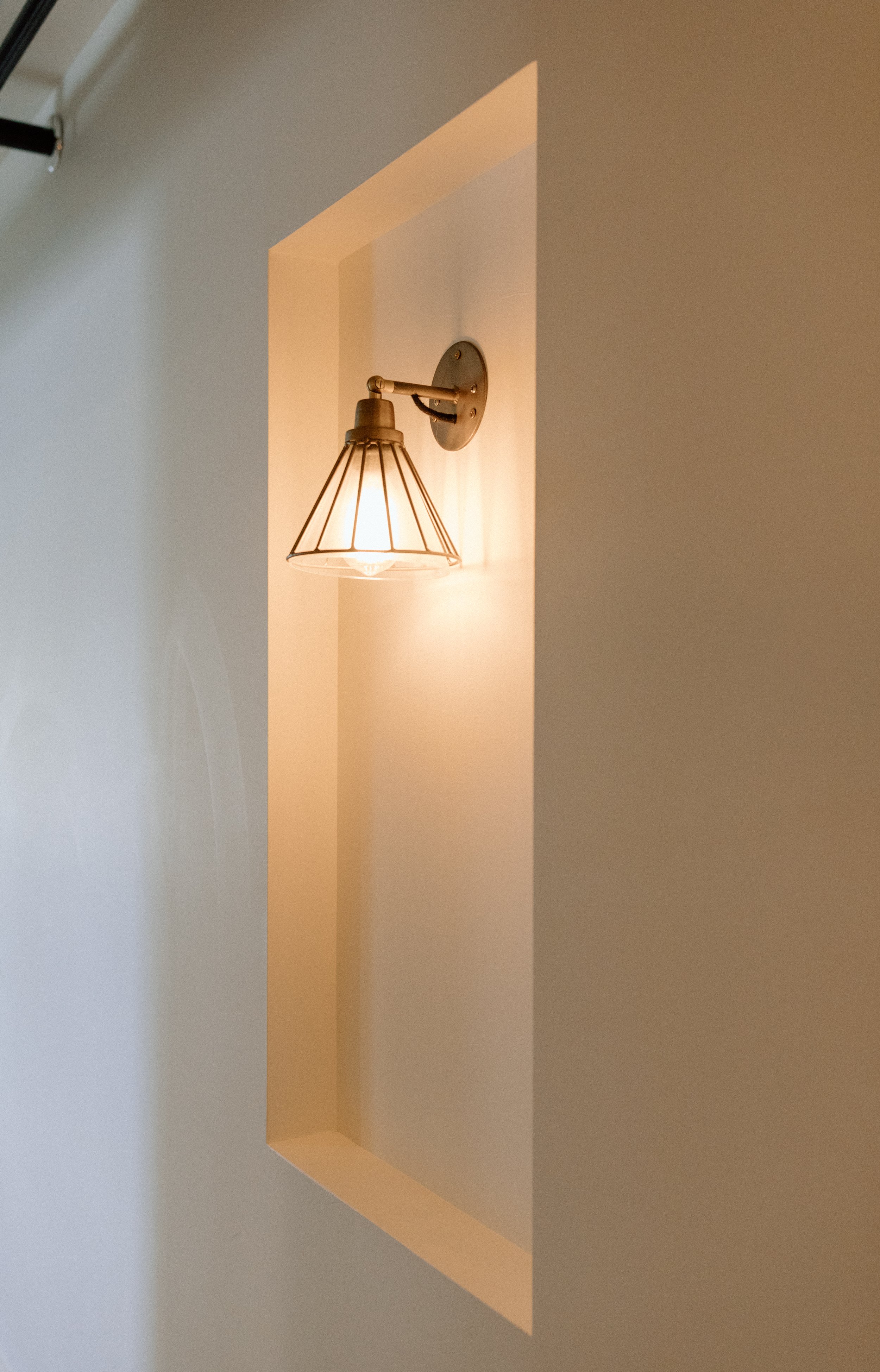 Wall-mounted industrial-style light fixture with a metal shade in a wall niche