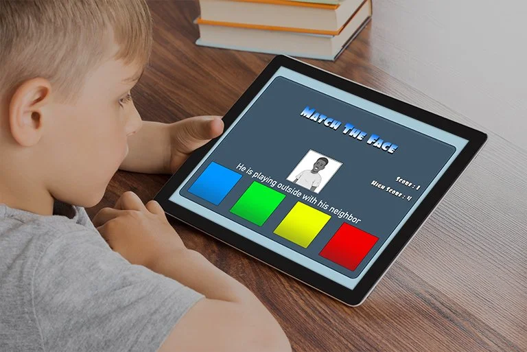 A young boy playing an educational face-matching game on a tablet, with colorful buttons and a cartoon face on the screen.