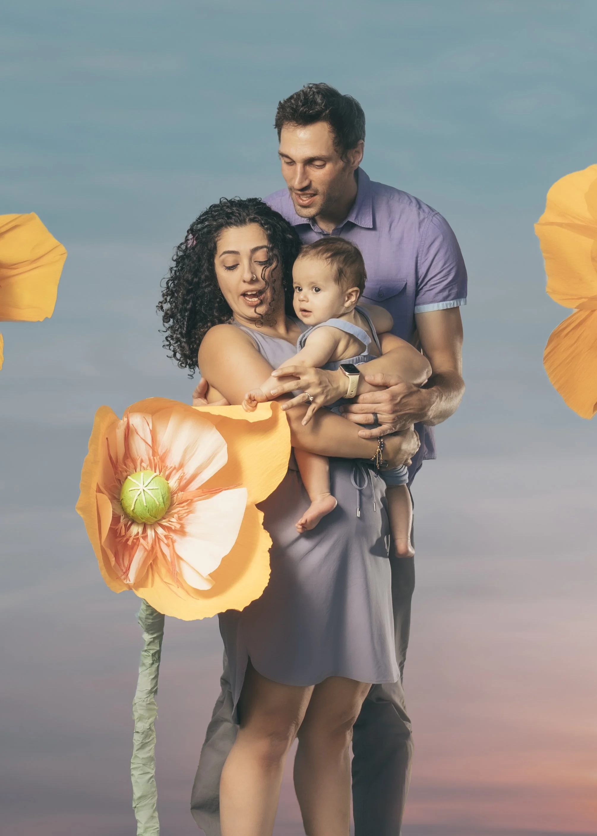A family of three holding a large artificial flower, standing outdoors against a sky background.