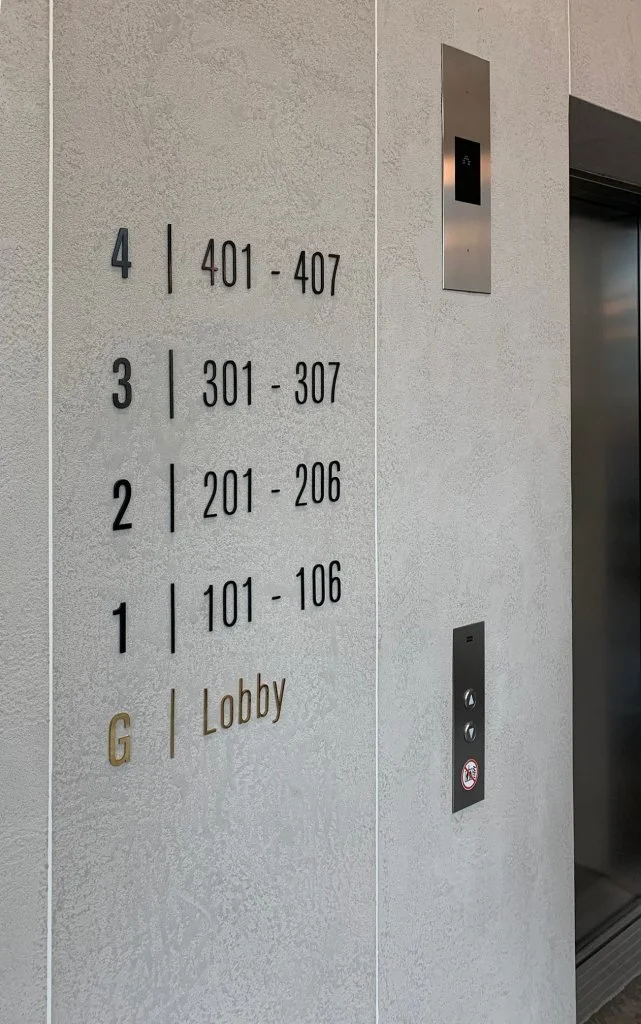 Elevator directory panel displaying numbered floors 1 through 4, basement G, and their respective room ranges, alongside elevator control buttons and a small display above for floor indication.