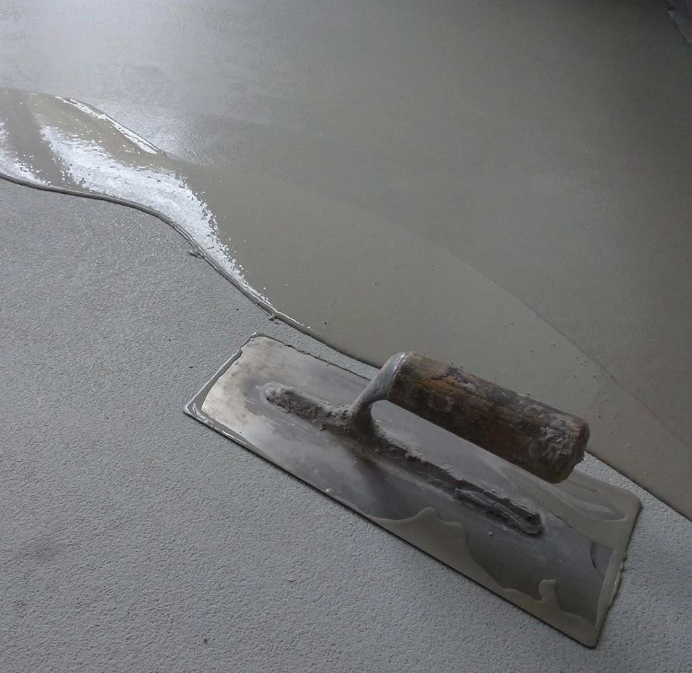 Flooring tools, including a trowel, are used to apply gray cement or mortar to a surface, with fresh cement in the process of setting.