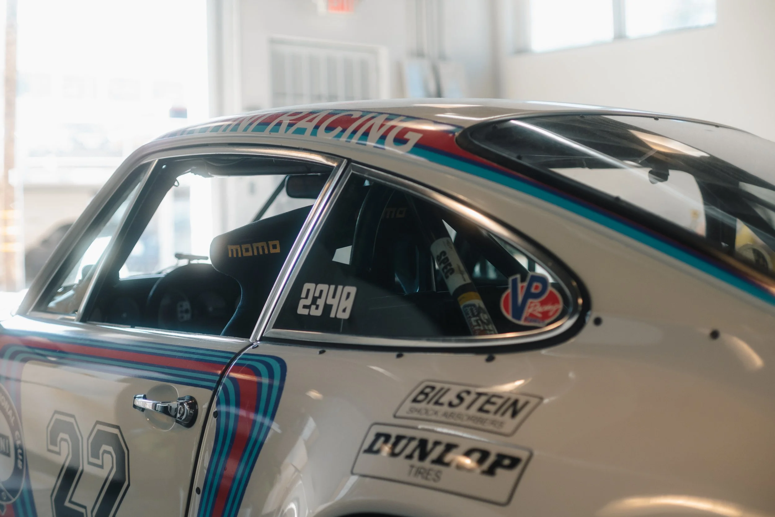 Close-up of a vintage race car with racing decals and a racing seat visible through the window.